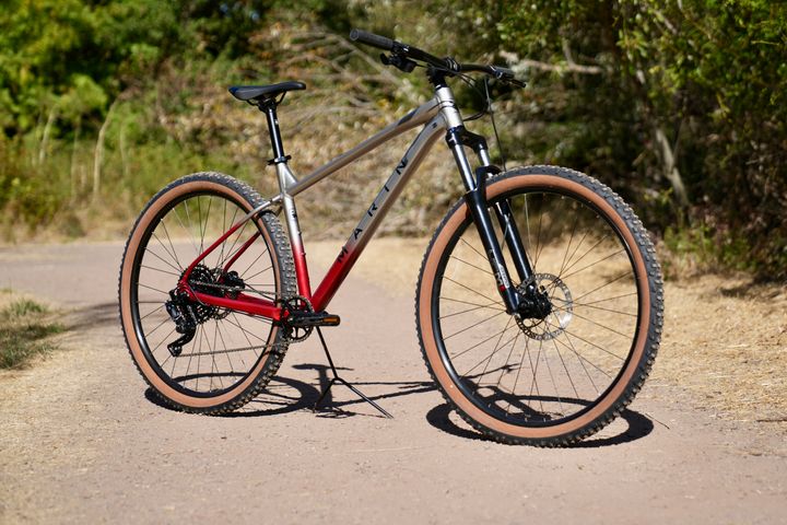 Marin Bobcat Trail 3 mountain bike close-up detail, showing frame and suspension components on a rugged trail background.